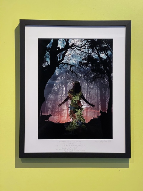 Framed picture of woman clad in leaves dancing among trees with black cats watching.