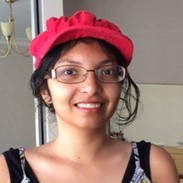 A young woman smiles in a headshot, wearing glasses and a bright red cap.